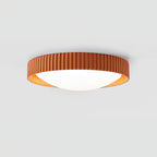 Orange Clérachic ribbed flush ceiling light seen from the side, its low profile and white diffuser lit on a pale grey backdrop.