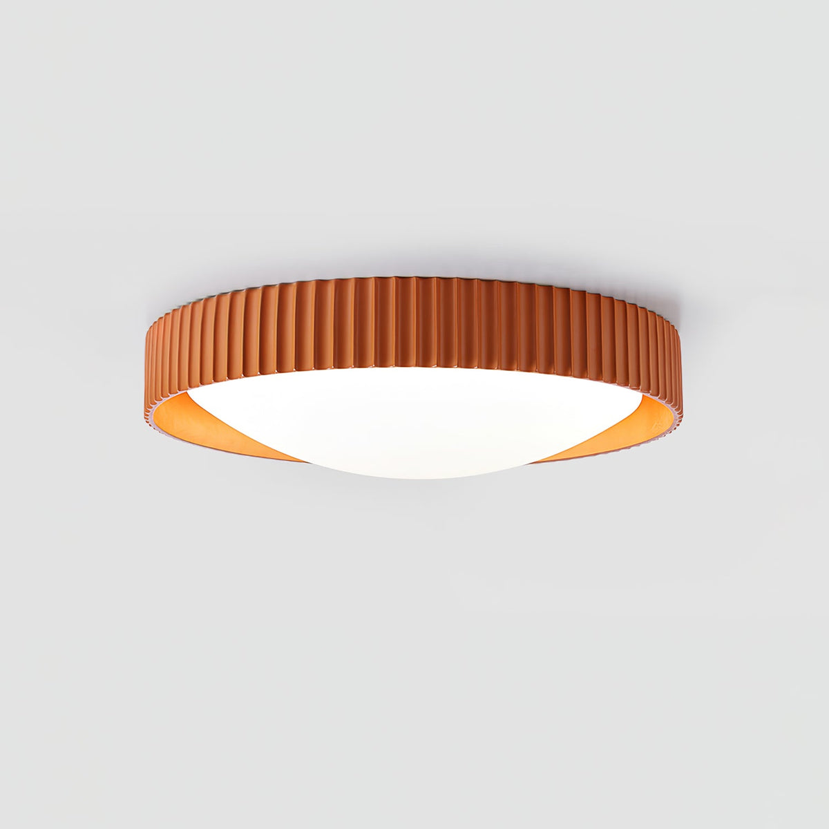 Orange Clérachic ribbed flush ceiling light seen from the side, its low profile and white diffuser lit on a pale grey backdrop.