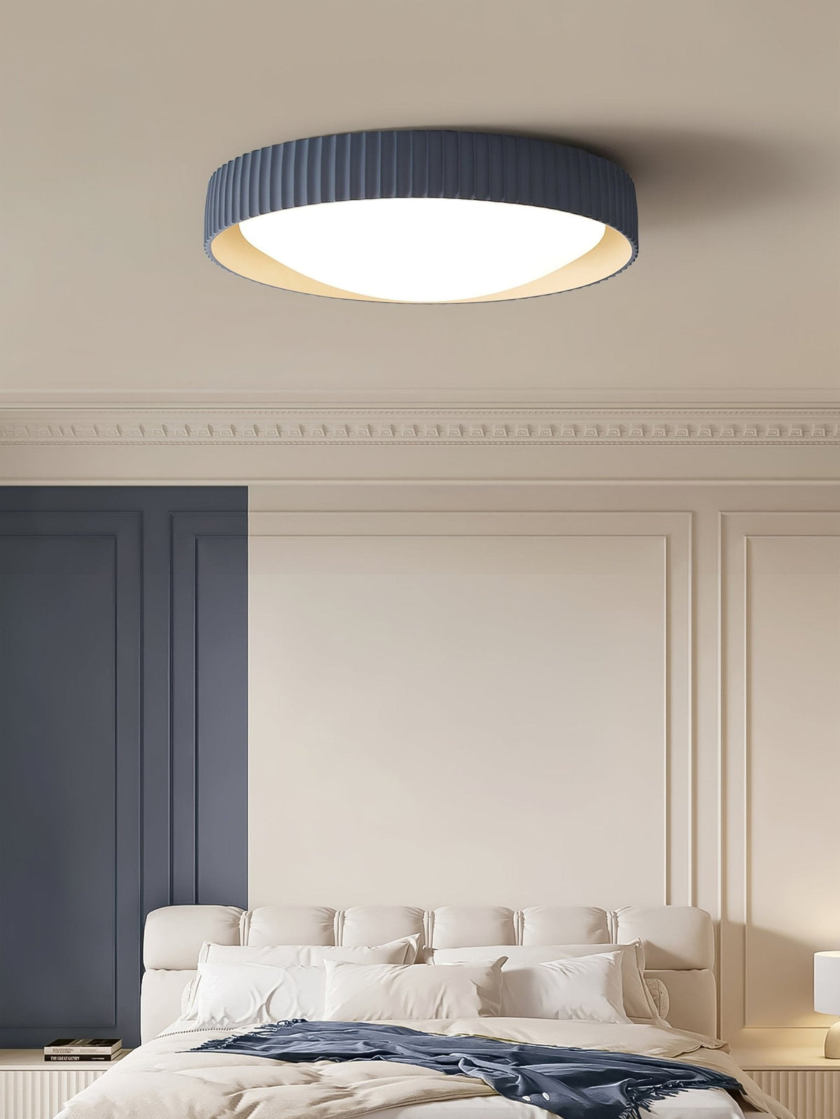 A blue Clérachic ribbed flush ceiling light above a white padded headboard, beside a panelled wall and a cornice.