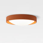 An orange Clérachic ribbed flush ceiling light on a plain white ceiling, shown from the side with its low profile and lit diffuser.