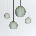 Clérachic ribbed opaline glass pendant lights in sage green shown as a cluster of four, staggered heights, unlit on white.