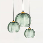 Clérachic ribbed opaline glass pendant lights in sage green grouped in three sizes, brass canopies, unlit on white.