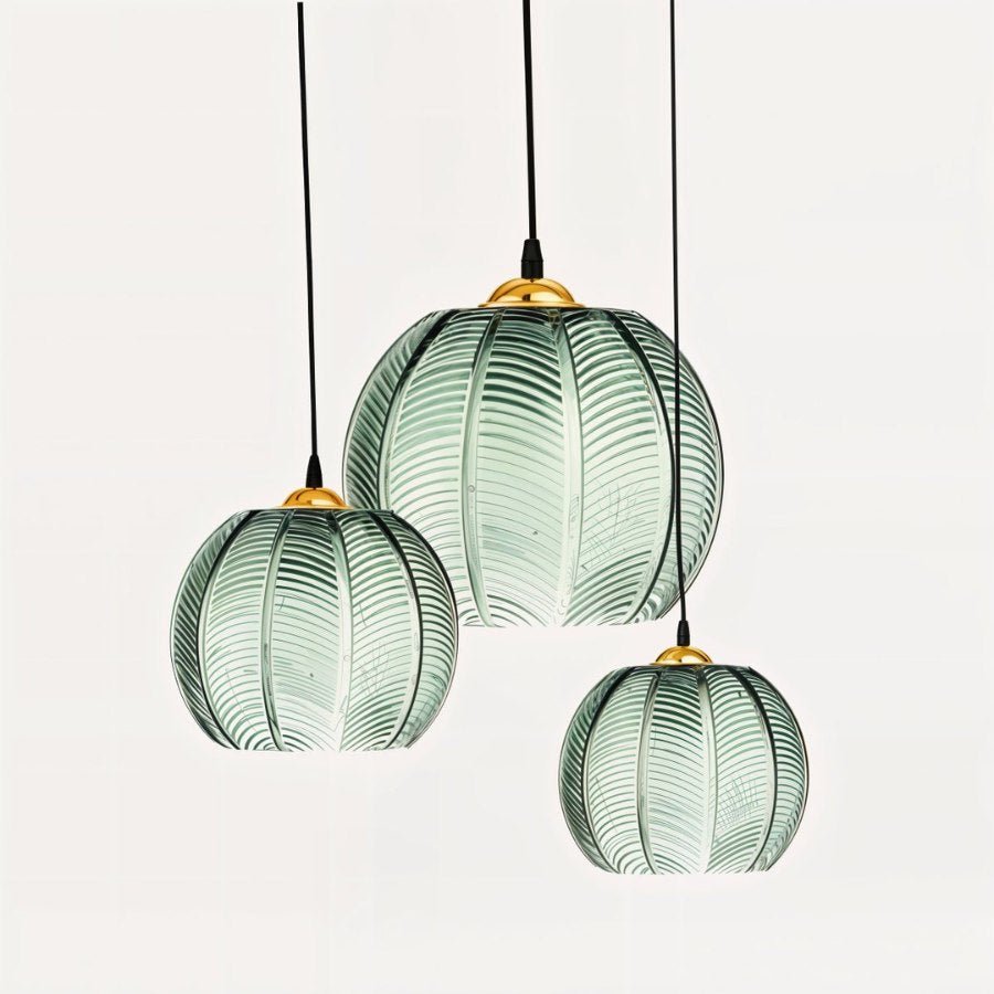Clérachic ribbed opaline glass pendant lights in sage green grouped in three sizes, brass canopies, unlit on white.