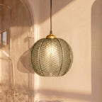Clérachic ribbed opaline glass pendant light in sage green glowing warm beside an arched glass shower in a bathroom.