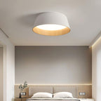White fluted Clérachic ceiling light with a wood-grain inner band, above a bed with a slatted headboard wall and soft strip light.