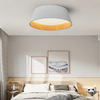 A white fluted Clérachic ceiling light above a bed with a pale timber headboard, with two framed prints on a grey wall.