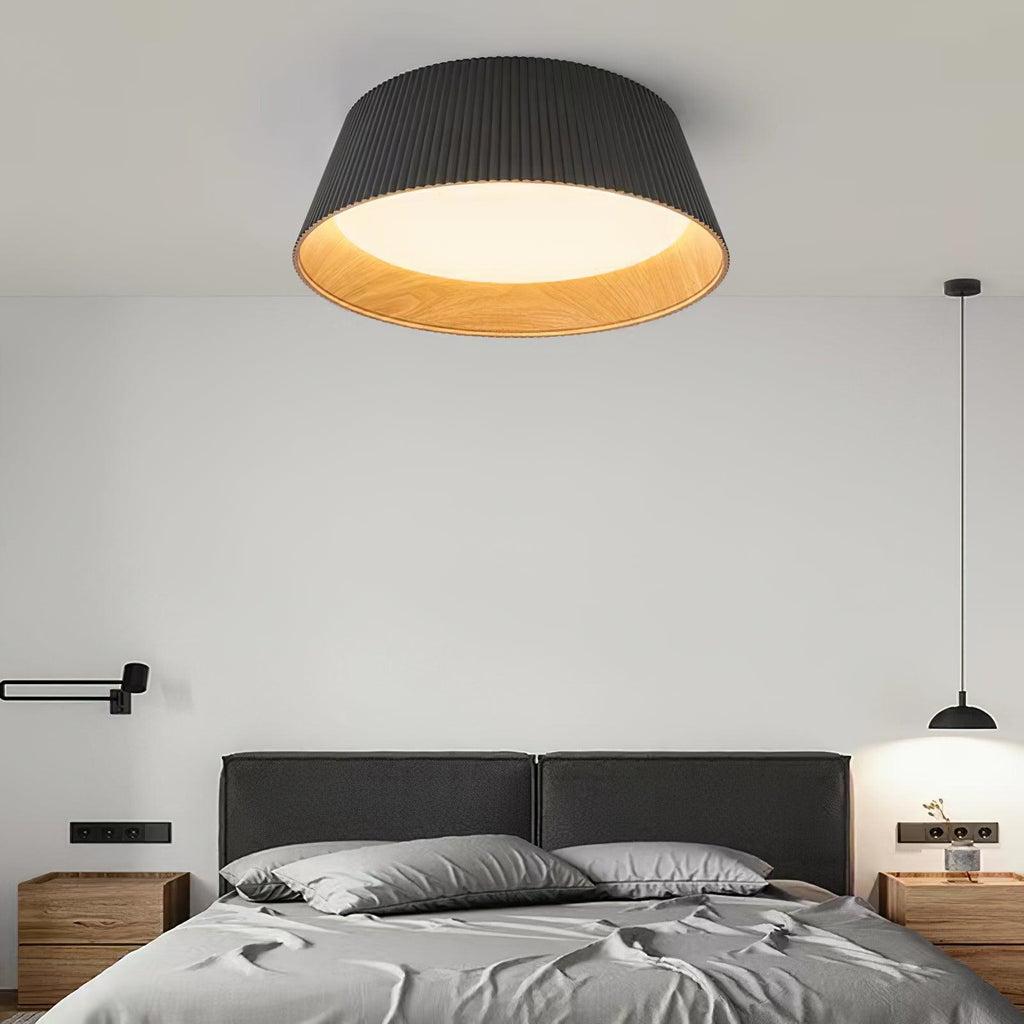 Black Clérachic ceiling light glowing above a grey bed with a dark headboard, wooden bedside tables and a black pendant at the side.