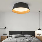 Black Clérachic ceiling light glowing above a grey bed with a dark headboard, wooden bedside tables and a black pendant at the side.