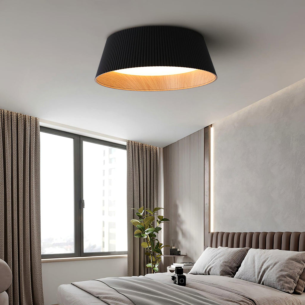 A black Clérachic ceiling light in a bedroom with a tall window, brown curtains and a ribbed headboard on a taupe wall.