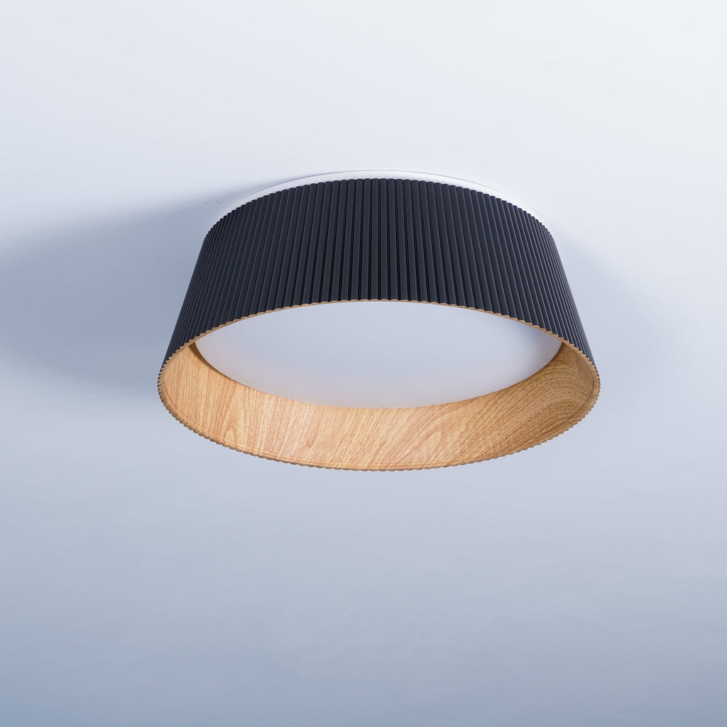 Black fluted Clérachic ceiling light against a pale blue-grey ceiling, its wood-grain interior catching the light.