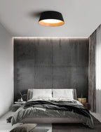 Black Clérachic ceiling light over a dark bedroom with a concrete-look wall, a grey bed and a curtain at the right.