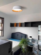 A white Clérachic ceiling light in a small bedroom with a dark headboard, a trailing green plant and open shelving.