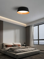 A black Clérachic ceiling light in a bedroom with a low grey bed, a concealed strip light and a large window.