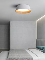 A white Clérachic ceiling light in a grey room, with a patterned blanket on the bed and teal cushions below.