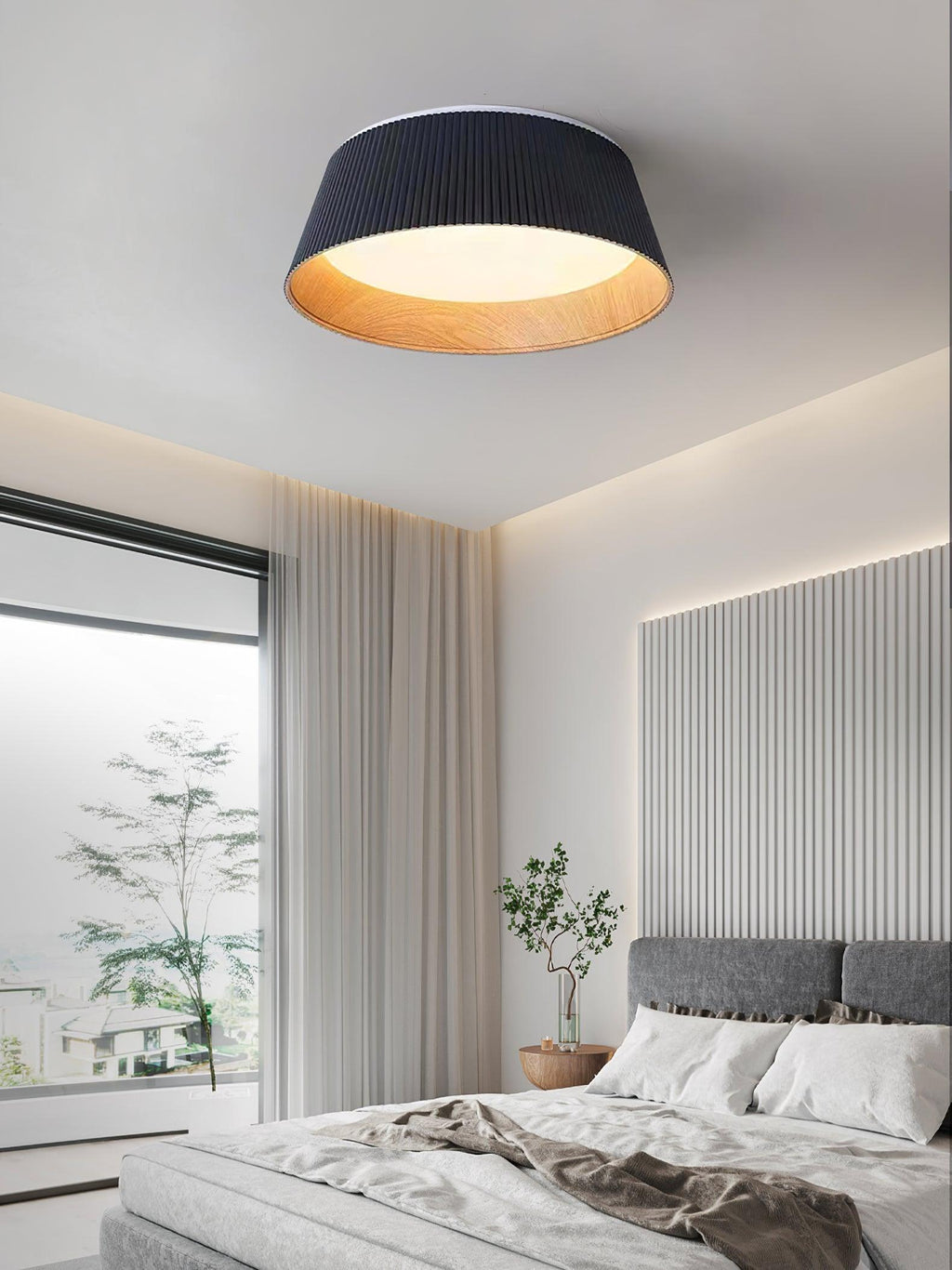Black Clérachic ceiling light above a bright bedroom with a grey bed, a potted plant and a fluted white feature wall.