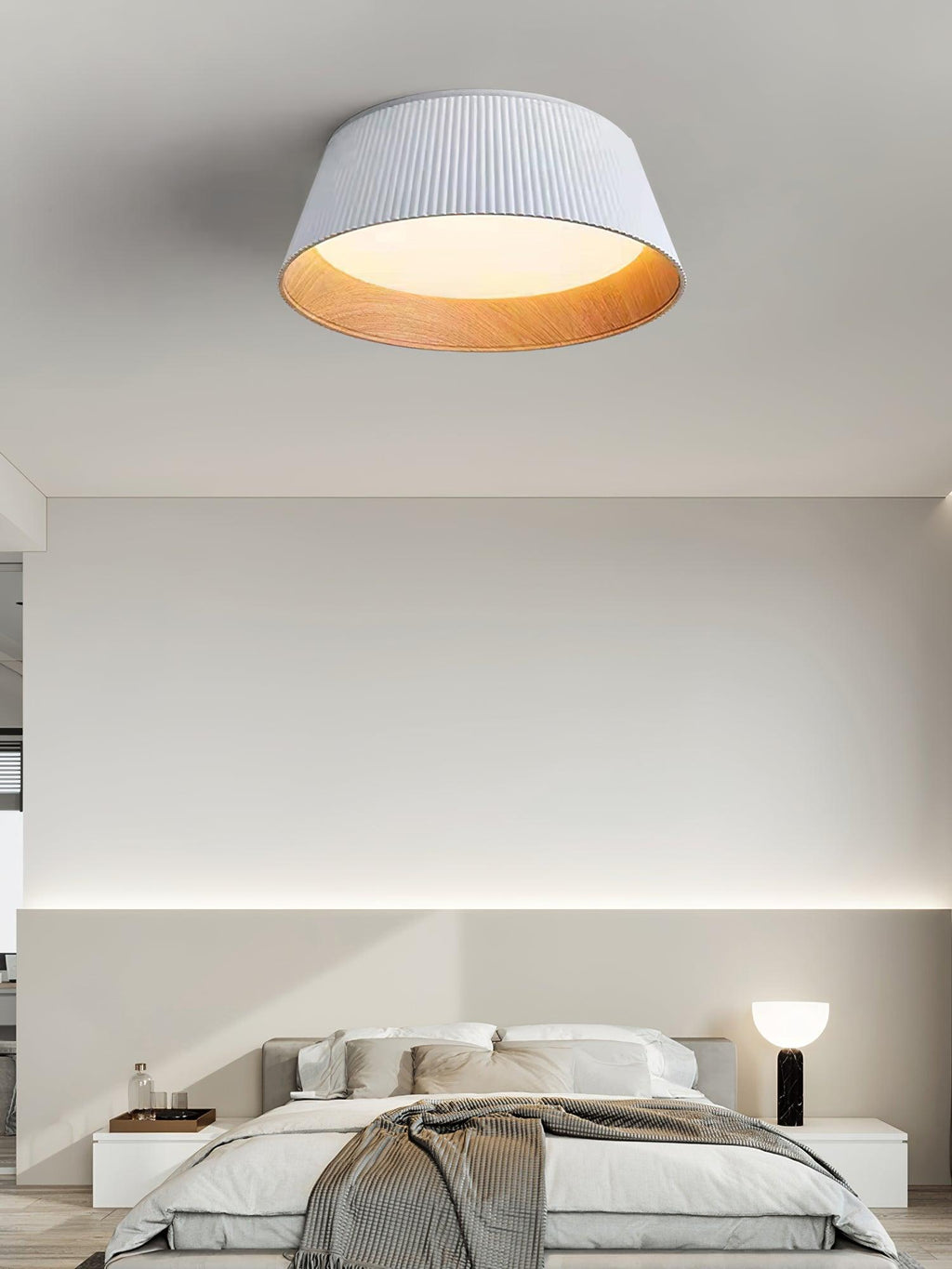 White fluted Clérachic ceiling light above a pale bedroom, with a black table lamp beside the bed.