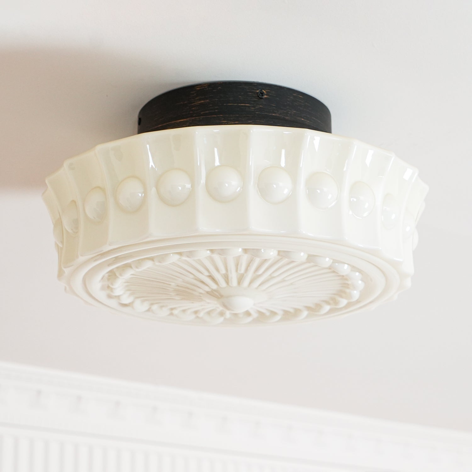 The white Clérachic fluted opal glass flush ceiling light with its round black ceiling canopy in close view.
