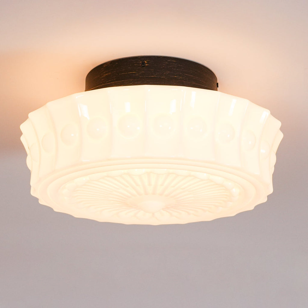 Close-up of the lit white Clérachic fluted opal glass flush ceiling light, casting a warm glow from its center.