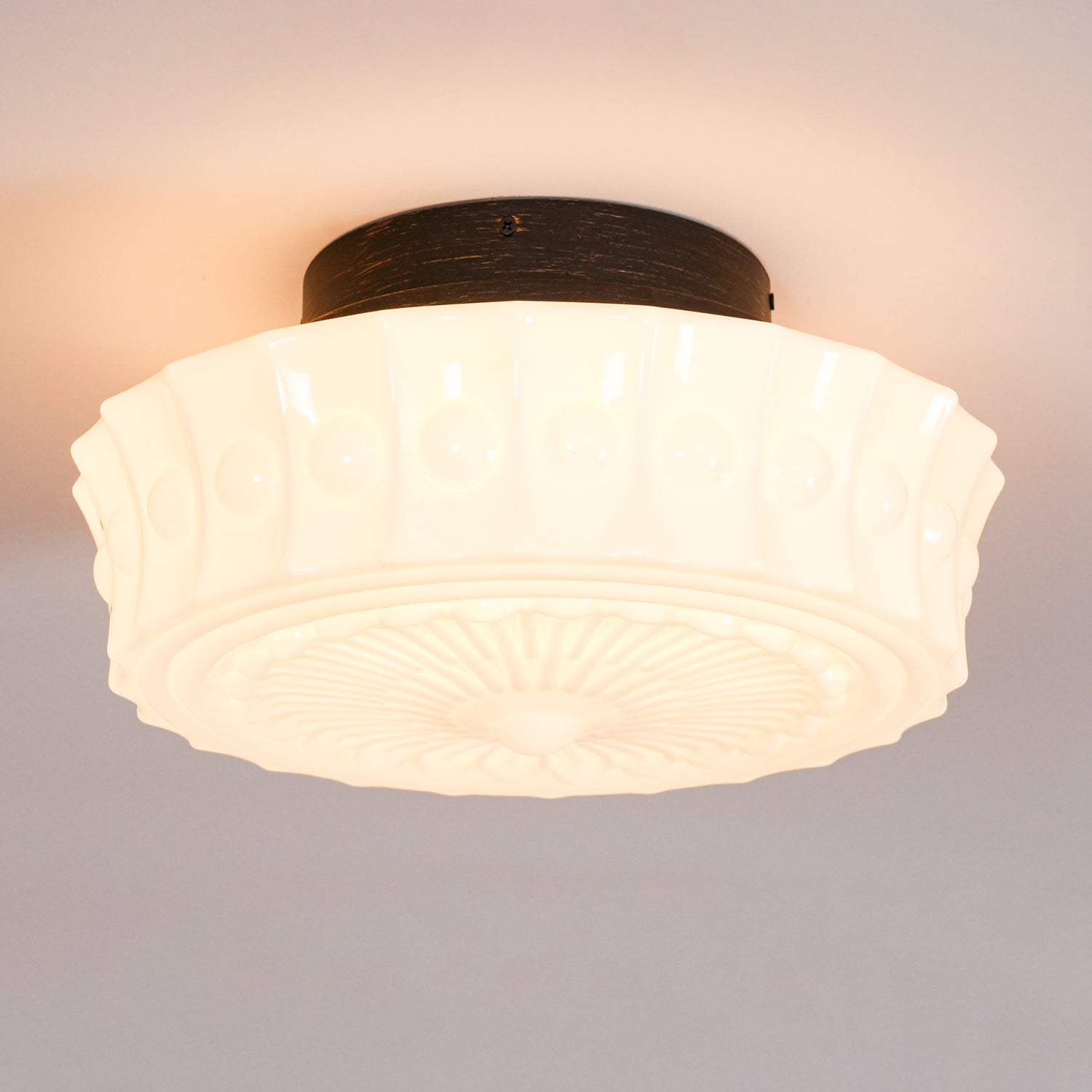 Close-up of the lit white Clérachic fluted opal glass flush ceiling light, casting a warm glow from its center.