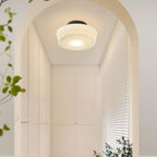 The white Clérachic fluted opal glass flush ceiling light lit in a plant-lined archway leading to a window.