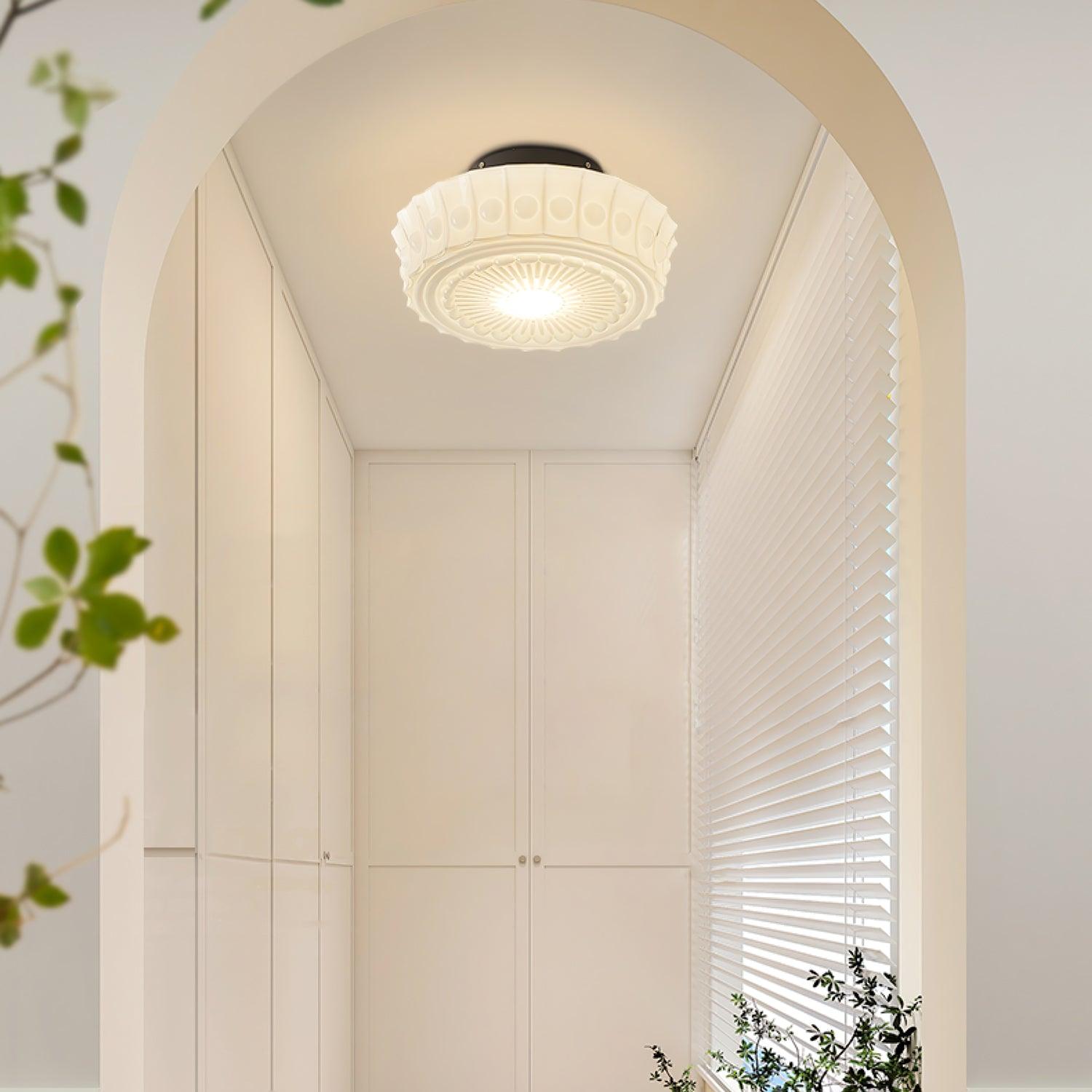 The white Clérachic fluted opal glass flush ceiling light lit in a plant-lined archway leading to a window.