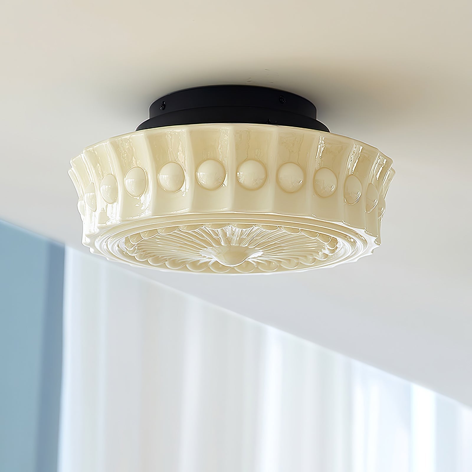 The beige Clérachic fluted opal glass flush ceiling light lit in a room with pale blue-toned window blinds.