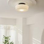 The white Clérachic fluted opal glass flush ceiling light lit beneath its fluted ceiling rosette, plants below.