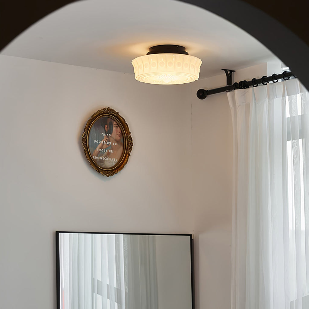 The white Clérachic fluted opal glass flush ceiling light lit in a room with an oval framed portrait and curtain rod.