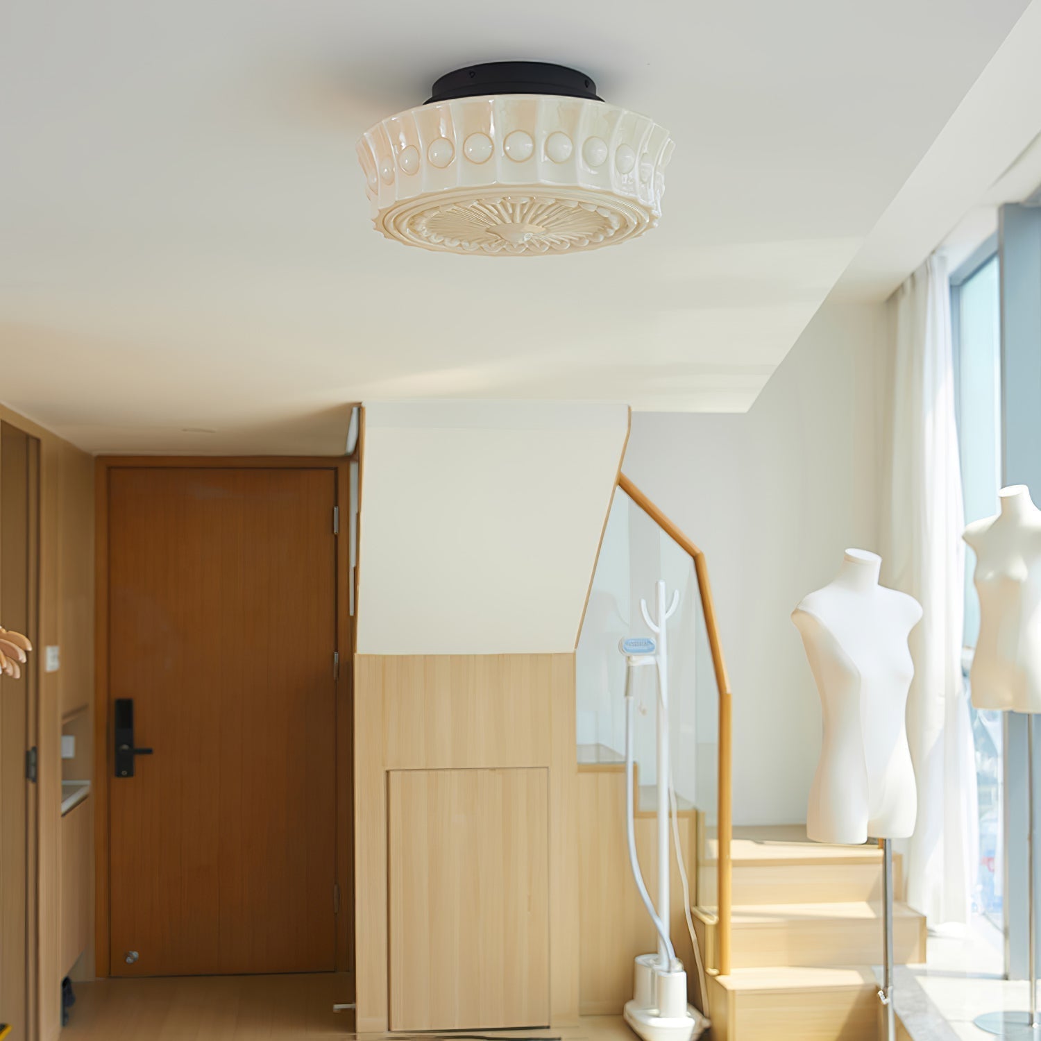The beige Clérachic fluted opal glass flush ceiling light lit in an entryway near a staircase and dress forms.