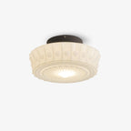 An angled studio shot of the beige Clérachic fluted opal glass flush ceiling light lit and glowing warmly.
