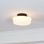 The white Clérachic fluted opal glass flush ceiling light lit in a room with plain walls and crown molding.