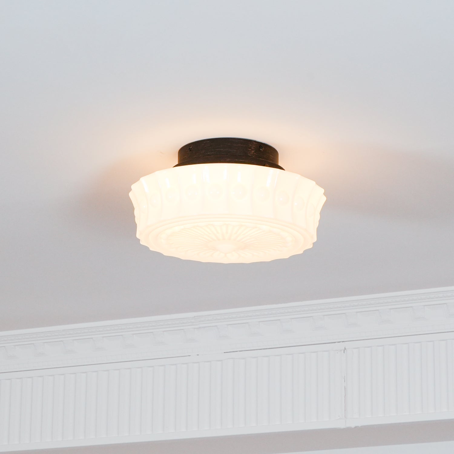 The white Clérachic fluted opal glass flush ceiling light lit in a room with plain walls and crown molding.