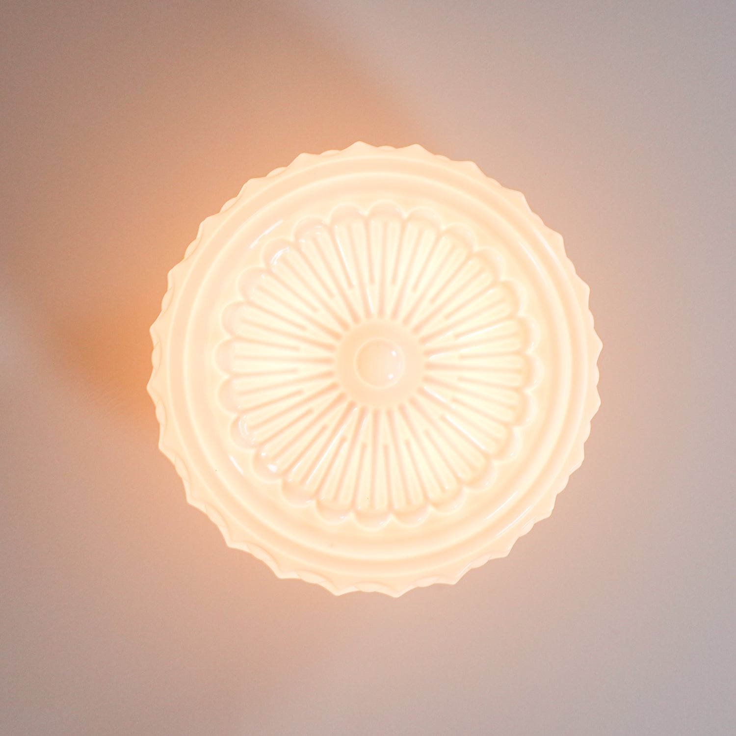 Extreme close-up of the lit white Clérachic fluted opal glass flush ceiling light's sunburst rosette underside.