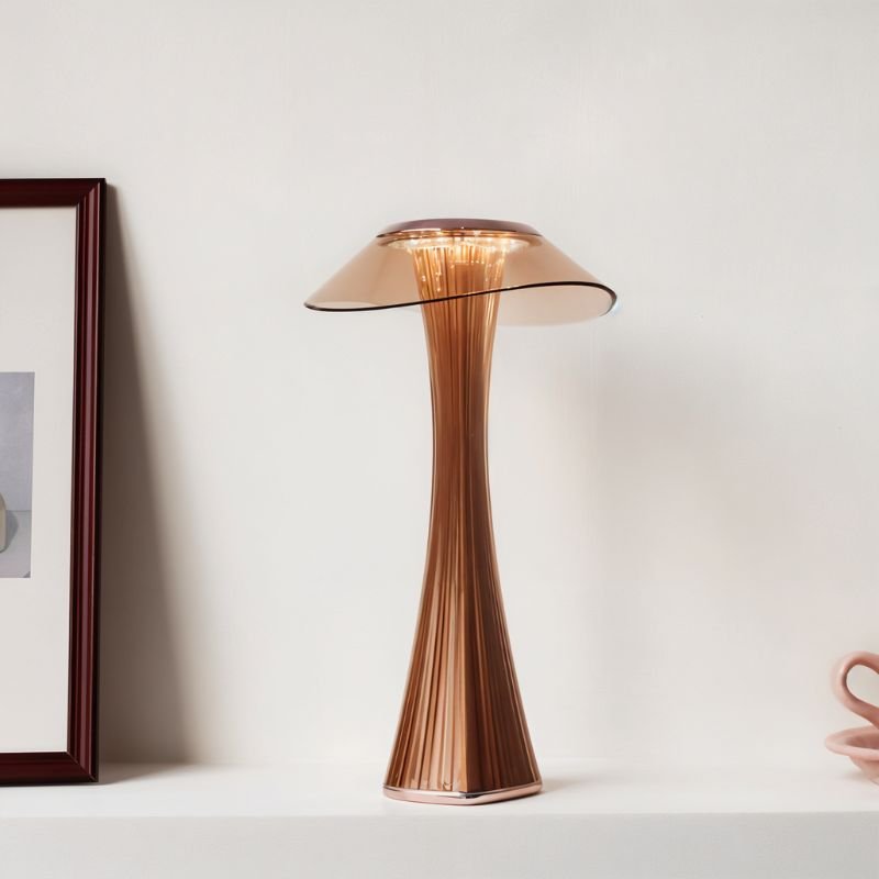 Clérachic bronze-toned fluted table lamp glowing on a white shelf beside a framed print and a pink cup
