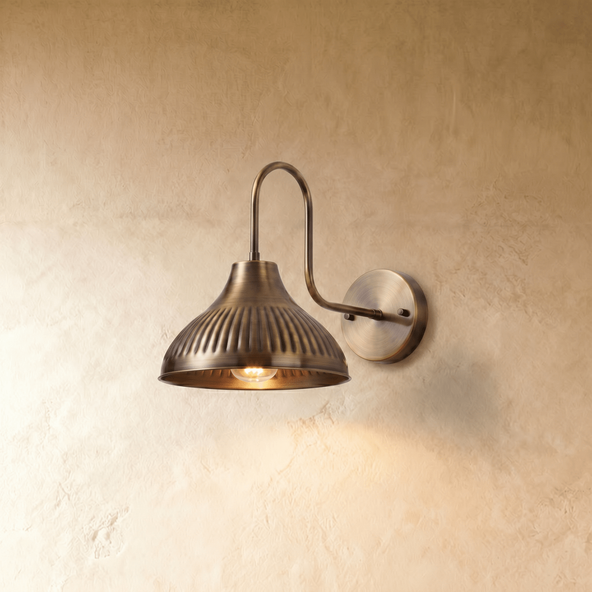 Clérachic wall lamp in vintage brass with a fluted dome shade on a swan-neck arm against a plaster wall.