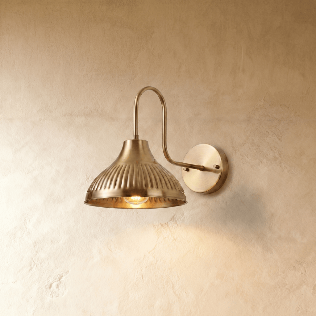 Clérachic wall lamp in polished brass, its fluted dome shade curving down from a gooseneck arm.