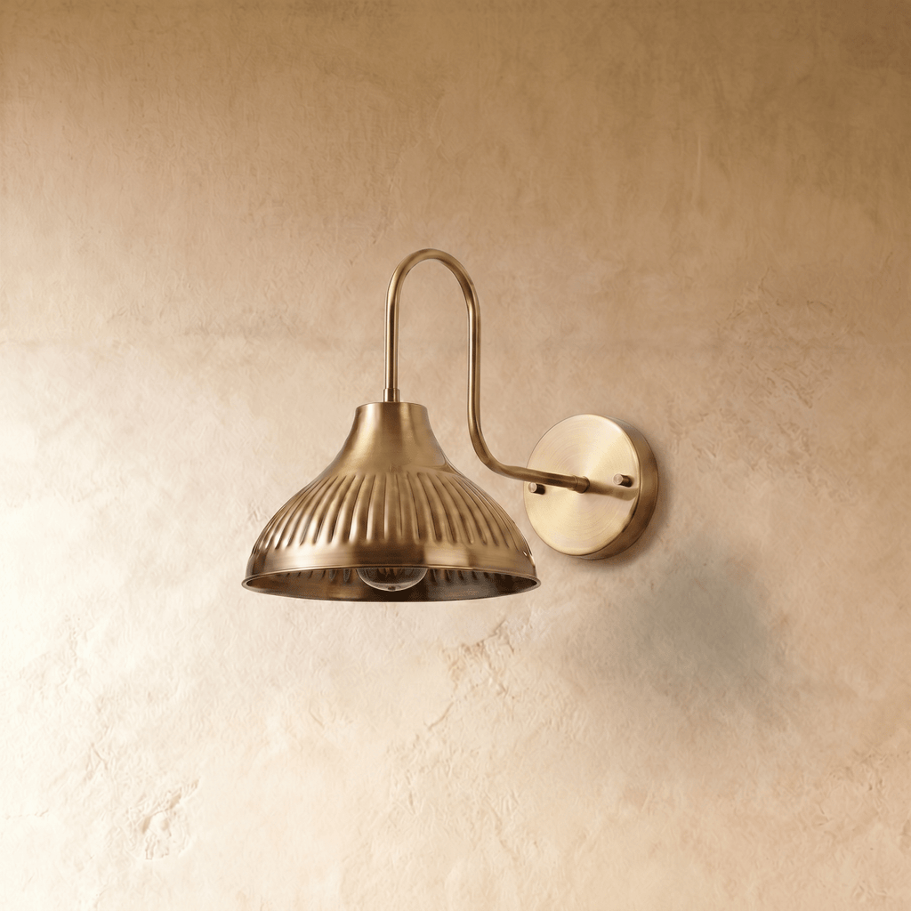A polished brass Clérachic wall lamp viewed from a different angle, the ribbed shade lit from within.