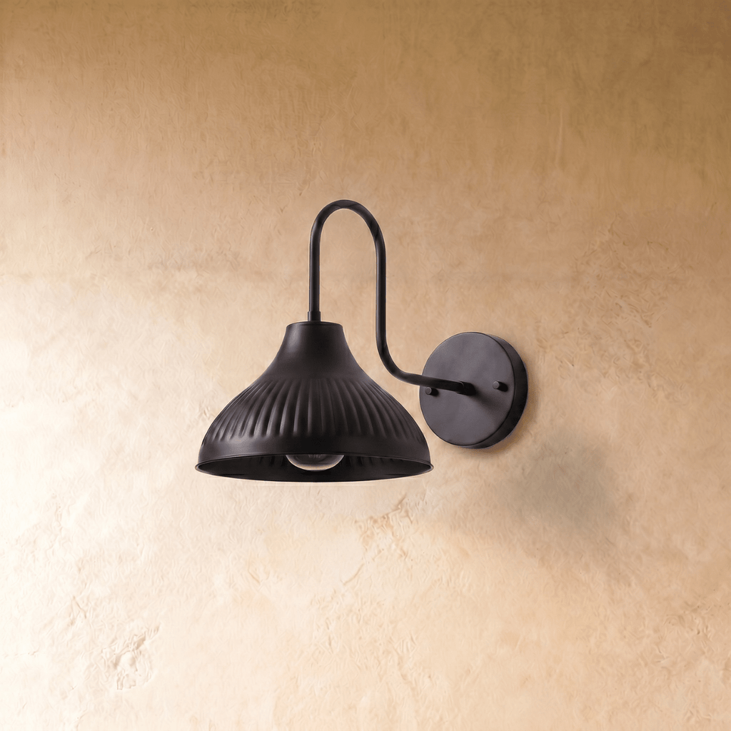 This black Clérachic wall lamp is shown from another angle, its ribbed shade glowing against the wall.