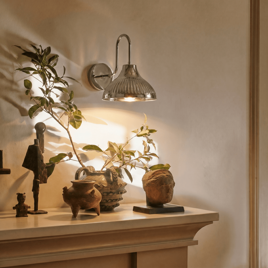 This chrome Clérachic wall lamp lights a mantel styled with small sculptures and potted greenery.
