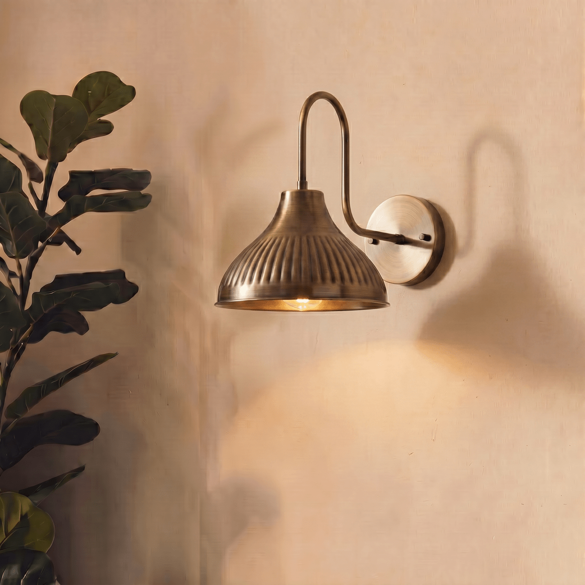 A vintage brass Clérachic wall lamp lights a living room corner beside a fiddle-leaf fig plant.