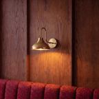 This brass Clérachic wall lamp lights a wood-paneled wall above a burgundy velvet banquette.