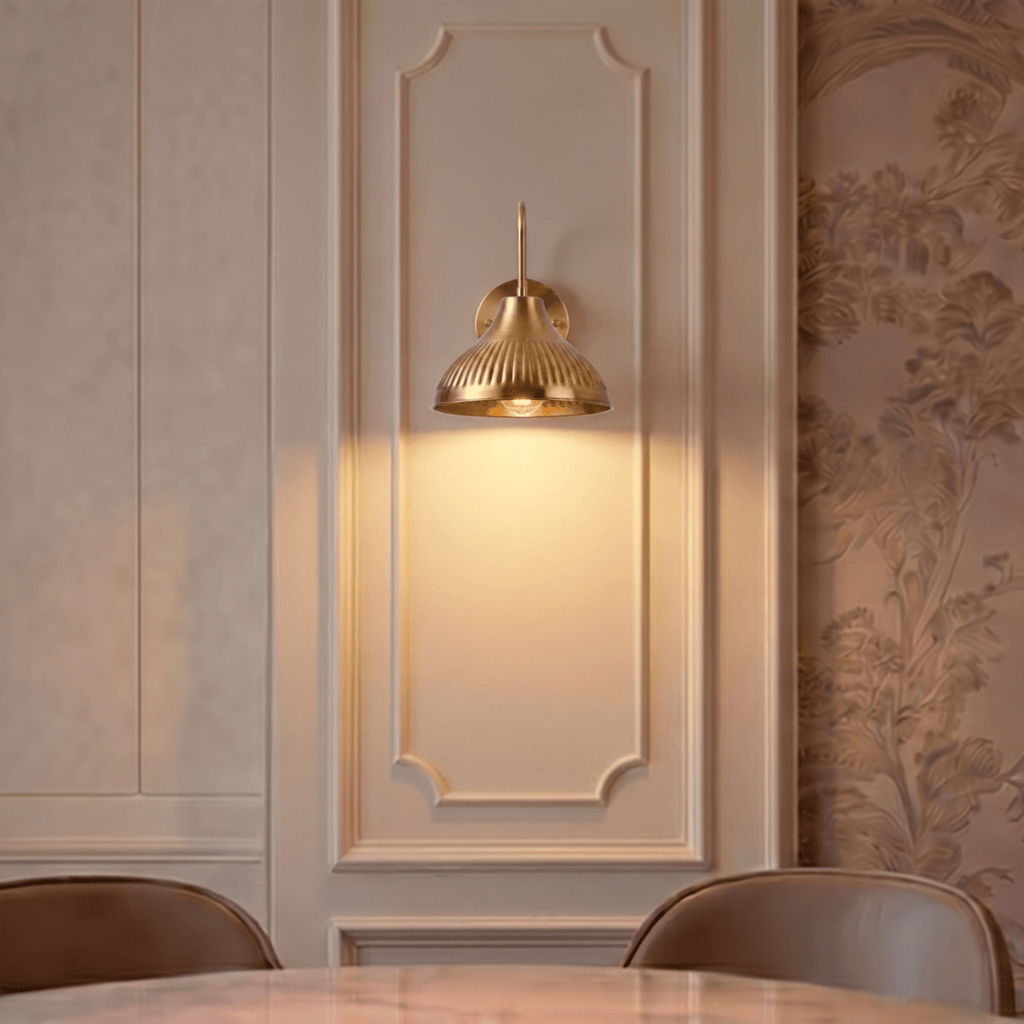 This brass Clérachic wall lamp lights a paneled dining room wall above a marble table and leather chairs.