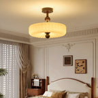 Ribbed cream disc shade lit warmly above a bedroom with a carved wooden bed, sheer curtains and framed bird prints, from Clérachic.