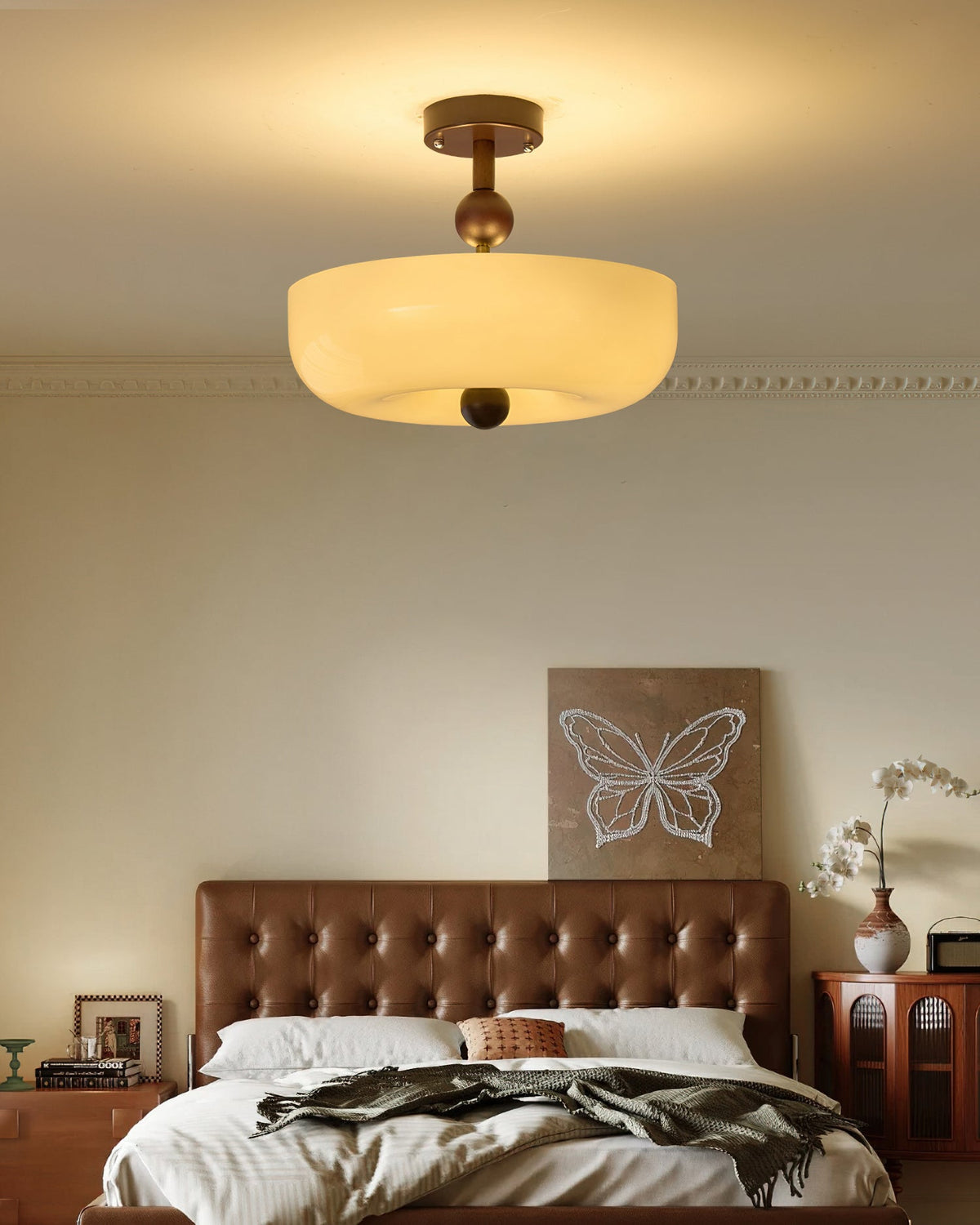 Smooth cream bowl-shaped ceiling light from Clérachic lit above a bedroom wall with a butterfly artwork and a leather headboard.