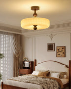 Lit fluted disc light from Clérachic below a corniced bedroom ceiling, with a wooden bed and floral bedding beneath.