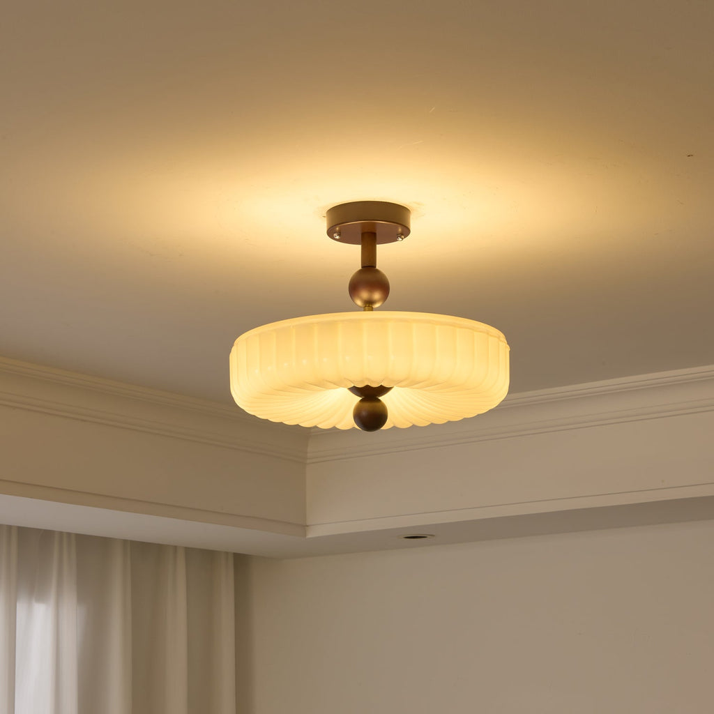 Ribbed disc ceiling light from Clérachic switched on, the fluted cream glass glowing above a corner of the room.