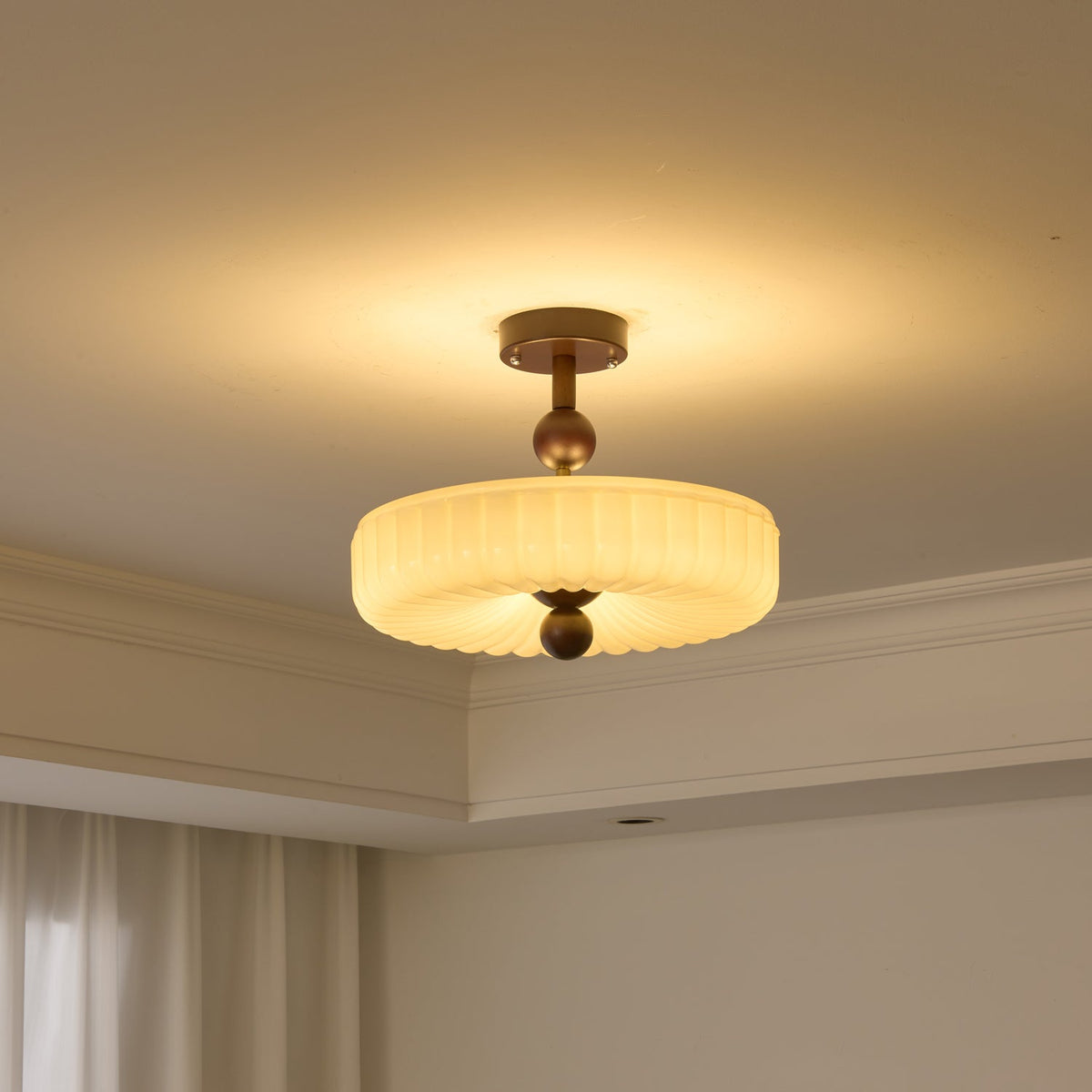 Ribbed disc ceiling light from Clérachic switched on, the fluted cream glass glowing above a corner of the room.