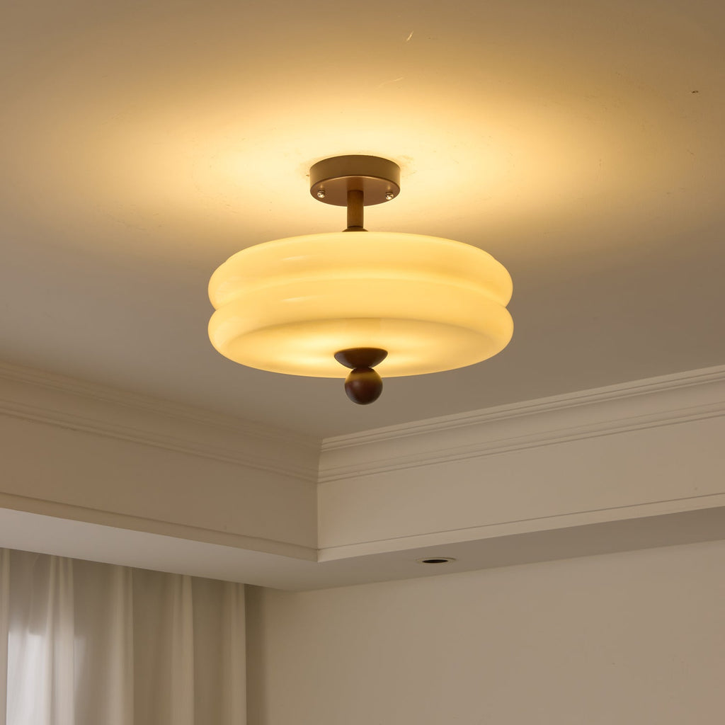 Lit double-tier cream shade from Clérachic, glowing yellow-white with a halo of light spreading over the ceiling.