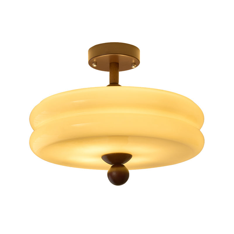 Close view of the double-tier cream glass shade and walnut ball tip of this Clérachic ceiling light, lit, on white.