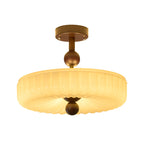 Fluted cream disc shade with radiating ribs below a walnut ball and stem, this Clérachic ceiling light lit, on white.